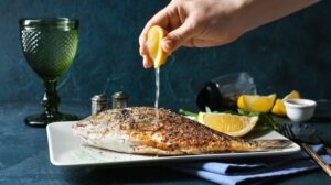 Hand pressar citron över en grillad fisk på ett fat